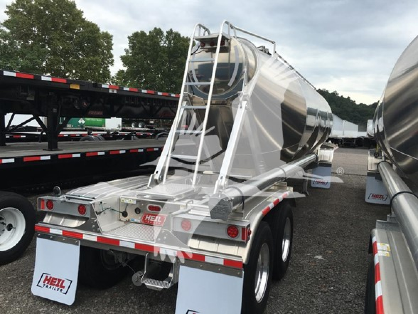 Trailer: Heil Cementer pneumatic dry bulk trailer, stainless steel tank with ladder and rear access, dual rear tires, reflective safety markings, mounted on a flatbed lot.