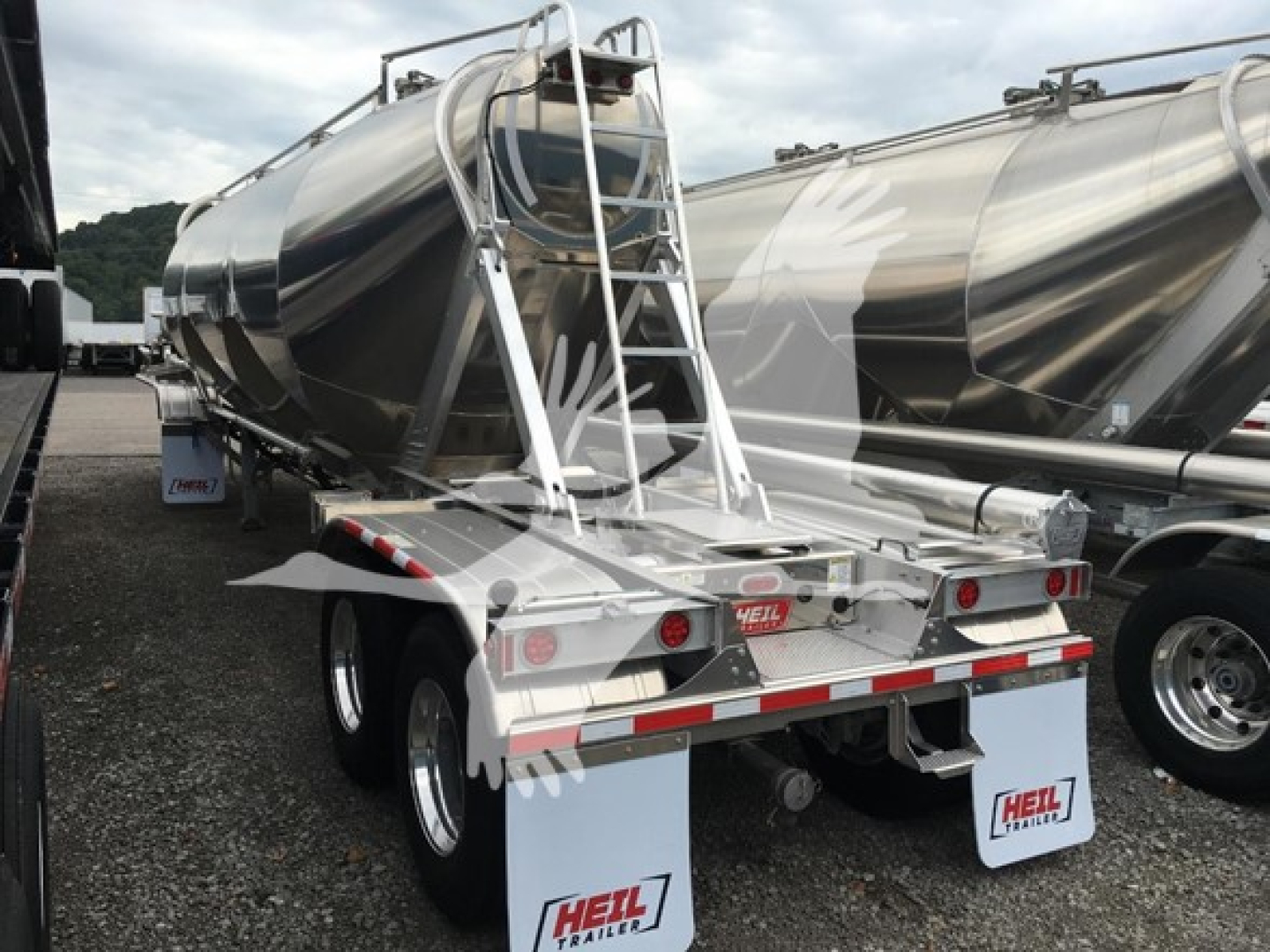 Trailer rear view showing Heil cement mixer/dry bulk pneumatic trailer with dual rear axles and white mud flaps, brand 'HEIL' on rear, aluminum-tank with ladder on top.
