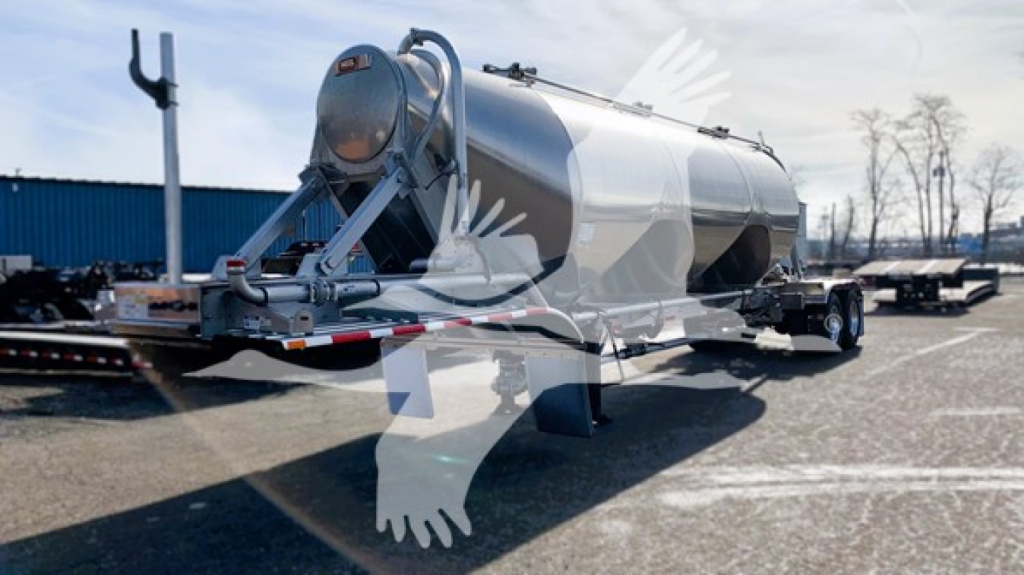 Pneumatic dry bulk trailer in a lot with a cylindrical tanker, dual-axle trailer, rear hitch and long chassis visible.