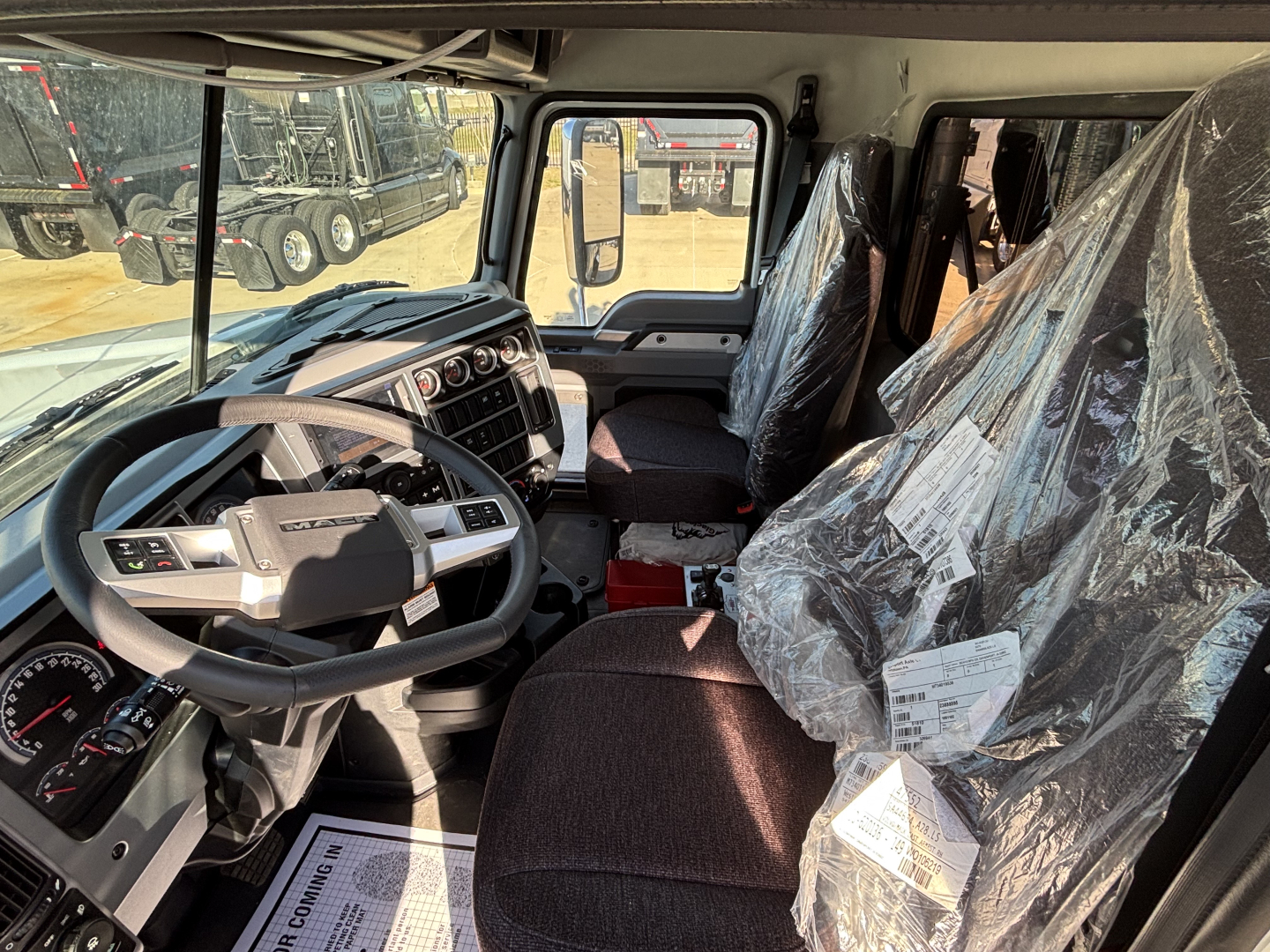 Truck cab interior of a 2026 Mack PI64 showing steering wheel, dashboard gauges, and plastic-covered seats.