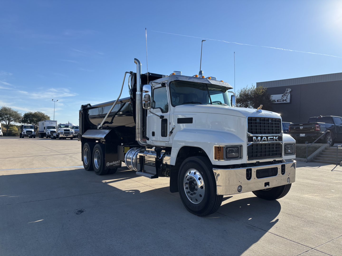 Mack PI64 dump truck in white and black, side view showing dump body and dual rear axles, chrome bumper, Mack grille, blue sky.