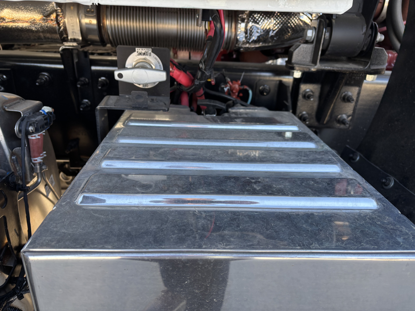 Mack PI64 engine bay with large metal toolbox/top cover and visible hoses, wiring, and hydraulic lines.