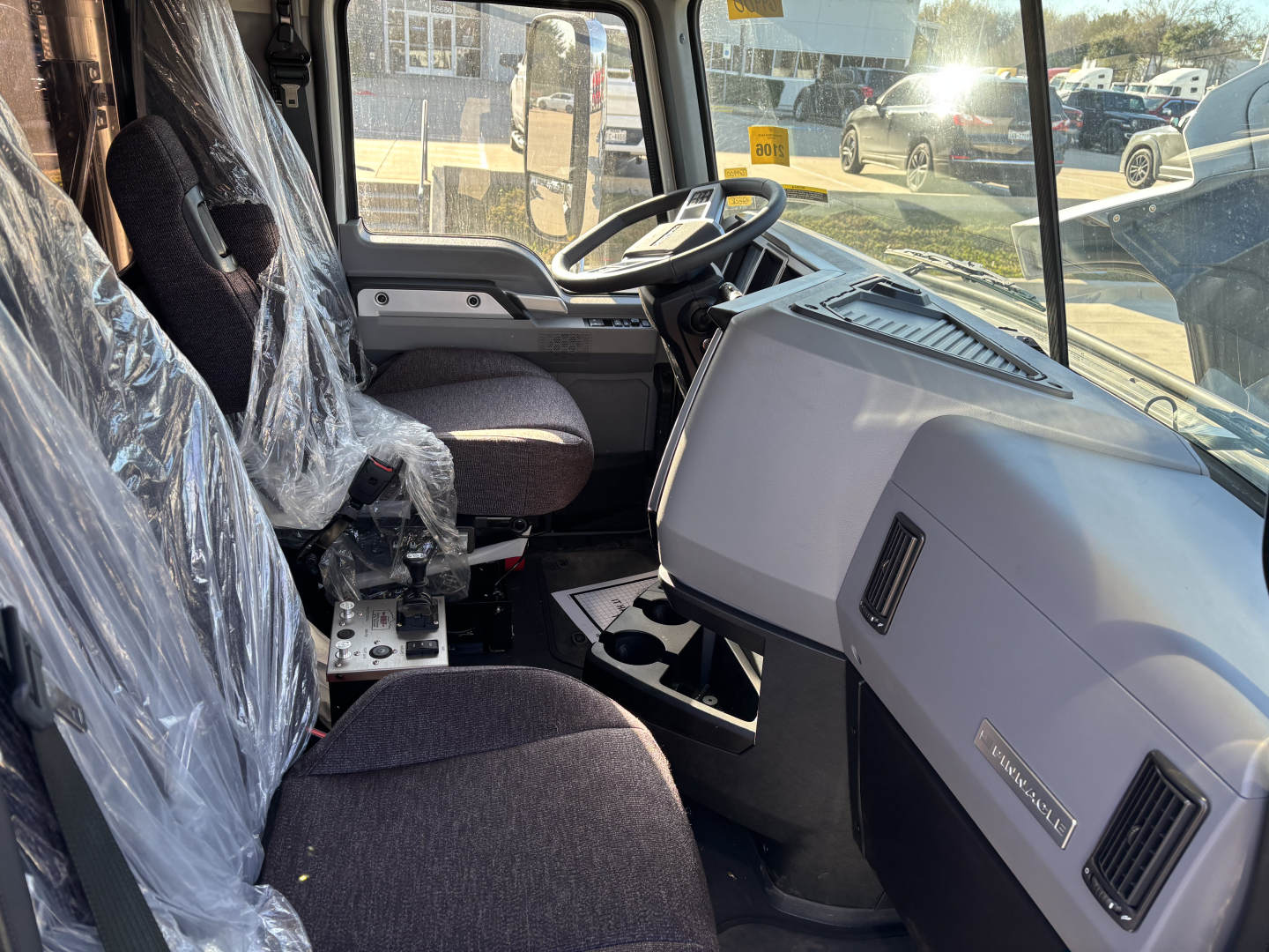 Truck interior showing steering wheel, dashboard, and driver seat of a new Mack PI64 dump truck.