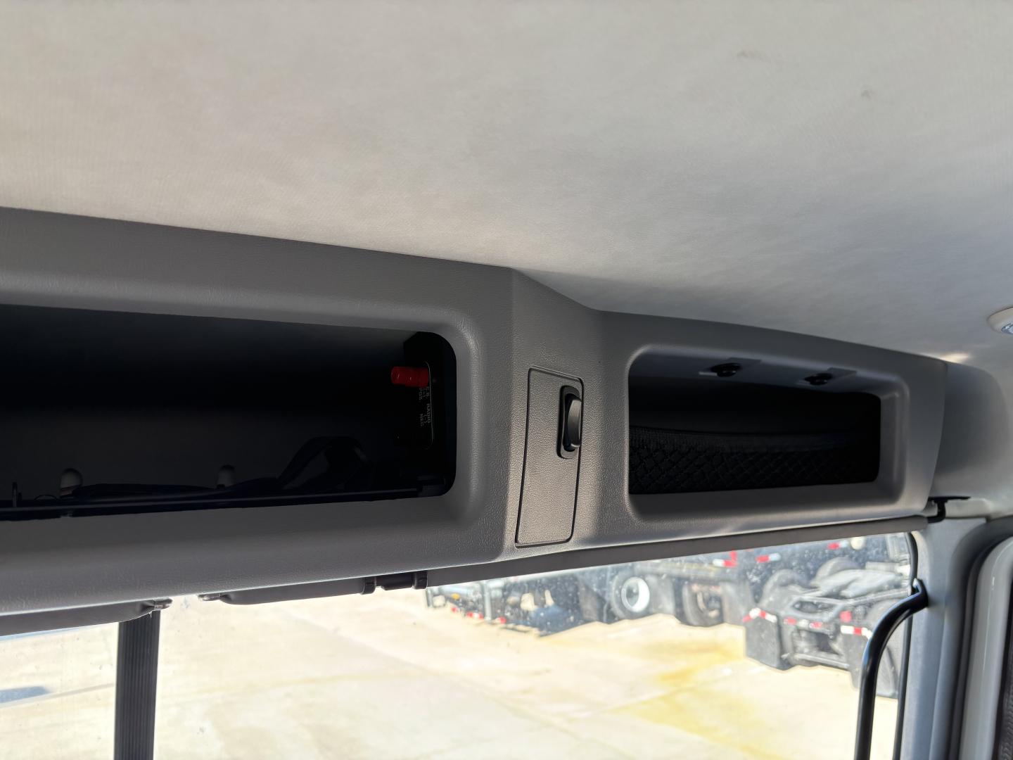New 2026 Mack PI64 dump truck interior showing overhead storage and dash vent area with a small red indicator and open compartment.