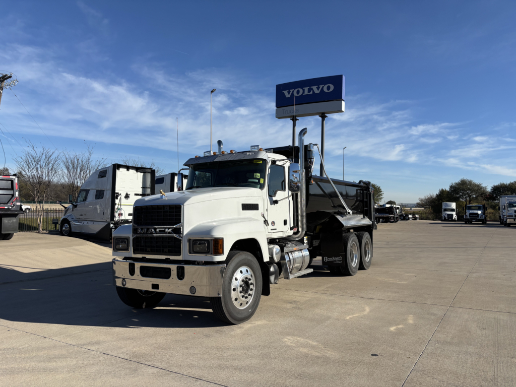 Mack PI64 dump truck in a dealership lot showing front view and dump bed.