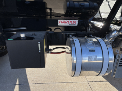 Truck side showing fuel tank straps and a black control box with a red cable nearby; chrome cylindrical tank with bands and a small label, 'HARDOX' sticker on the frame.