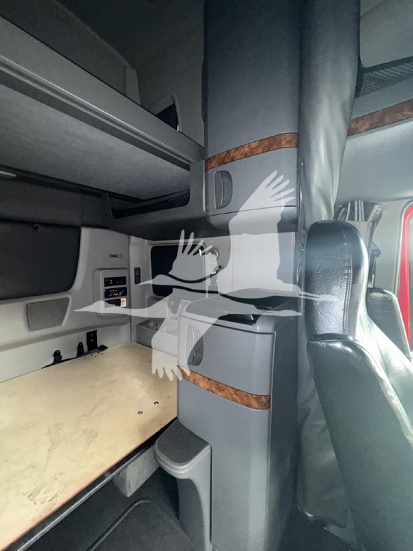 Cockpit interior of a 2019 International LT truck showing a sleeper cab area with wood trim and a plywood bunk surface.
