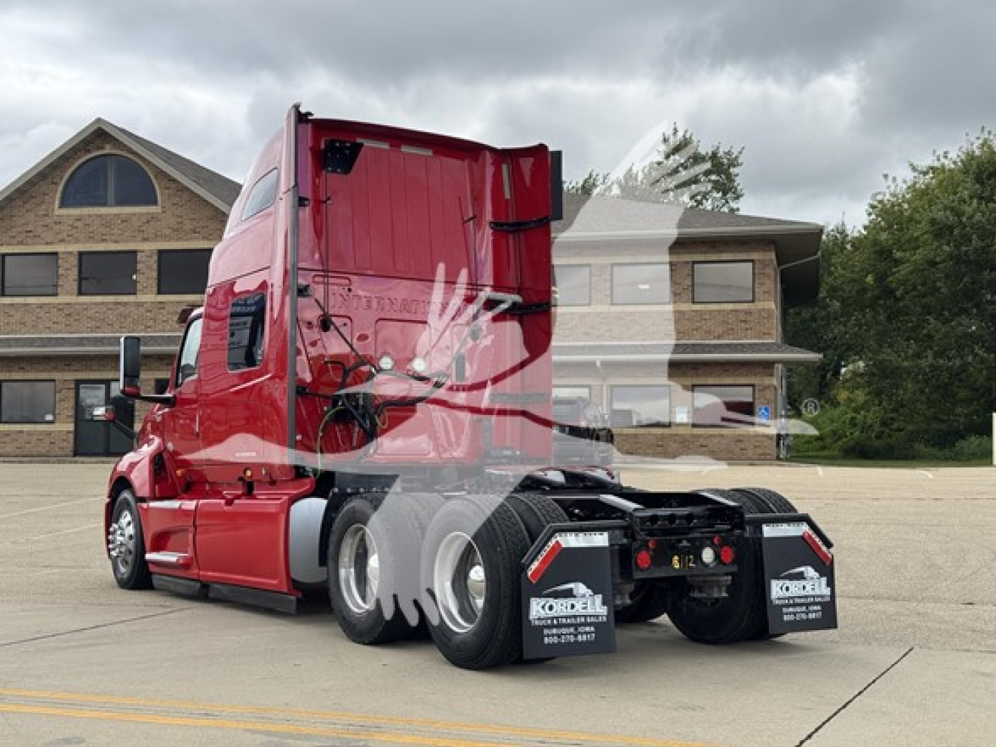 Tractor unit in red color, side rear view showing sleeper cab and dual rear axles with maroon chassis and black mud flaps.