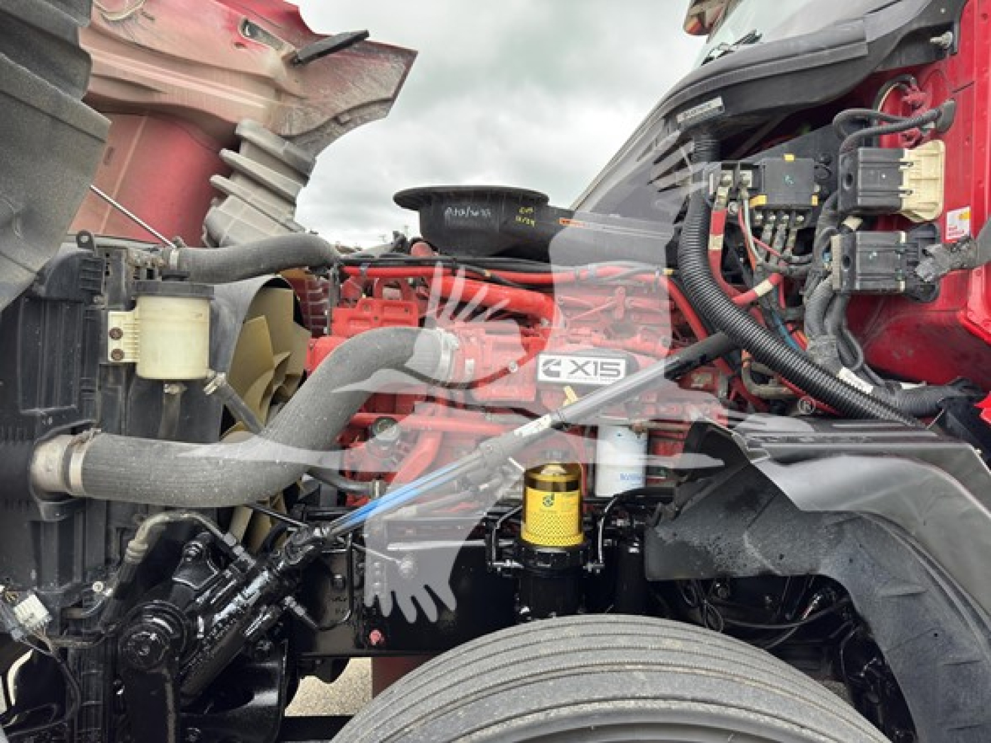 Truck engine bay of a 2019 International LT showing components: air intake hoses, coolant reservoir, yellow oil/filter, wiring harnesses, and engine block with X15 label.