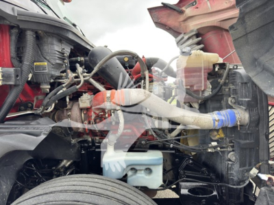 Truck engine bay with coolant reservoir, hoses, and air intake visible in the front; various engine components and tubing in view.