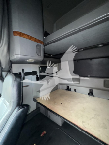 Cab interior showing sleeper bunk area with a wooden table surface, overhead cabinet, and partial seat in foreground.
