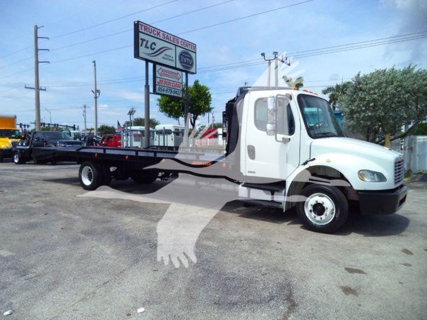 Flatbed tow truck in a lot showing Freightliner M2 106 cab and chassis with long flatbed.