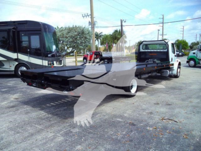 Flatbed tow truck with a black flatbed, Freightliner M2 106 style cab in background, VIN tag not visible, stock number TBP9505. Side view shows long hex frame and wheel configuration.
