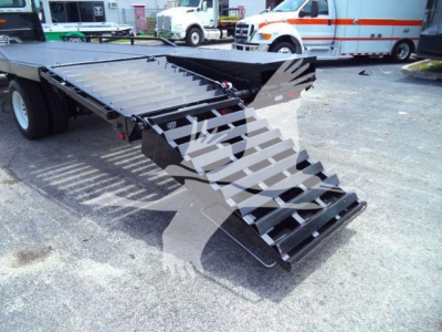 Flatbed truck with foldable ramp on a Freightliner M2 106 trailer deck showing metal steps and hydraulic latch in a yard.