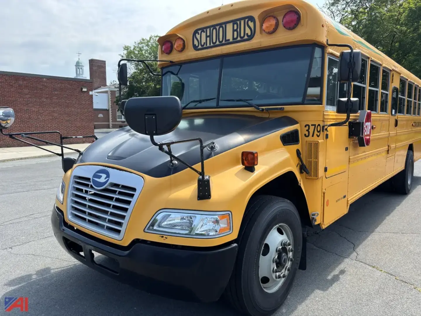 School bus front quarter view showing yellow body, black bumper, and side mirrors; 'SCHOOL BUS' sign atop windshield and rearview cameras; number 379 on front fender.