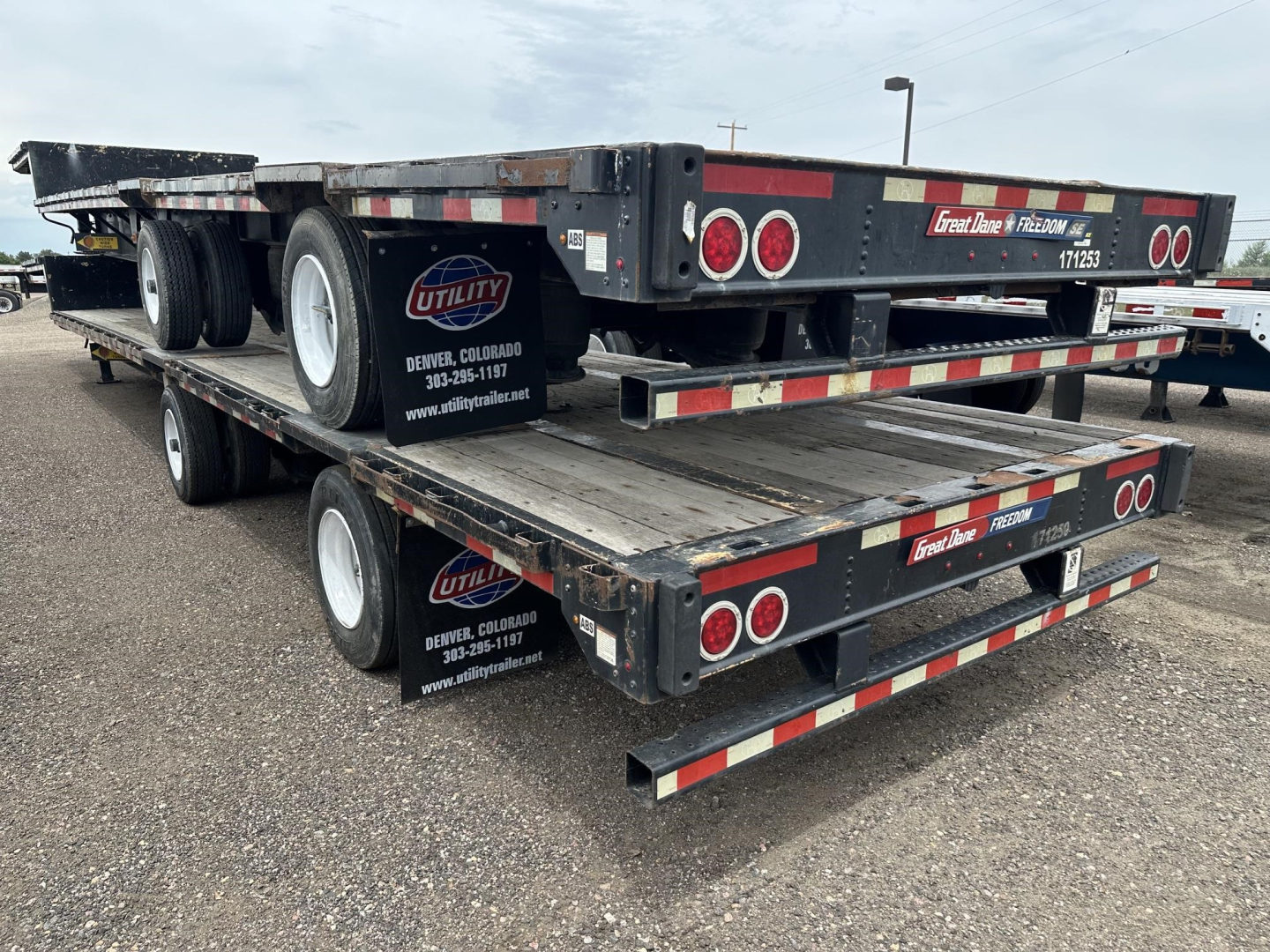 Flatbed drop deck trailer stacked on two levels with branding and reflective tape, Utility logo visible, Denver Colorado contact