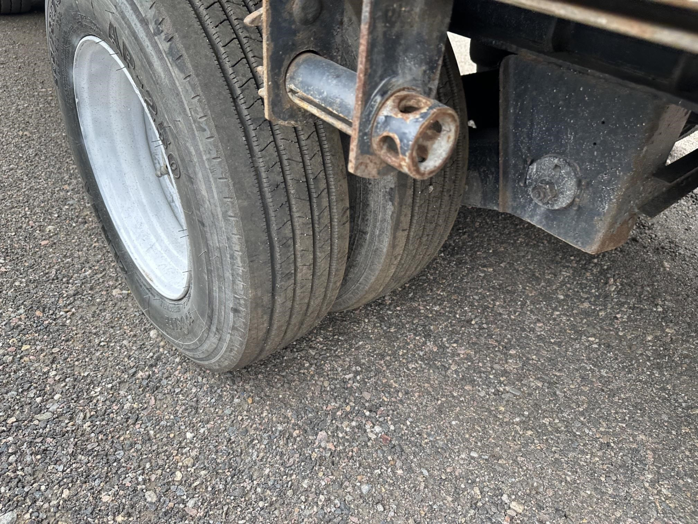 Dual rear wheels of a Great Dane trailer axle assembly with rusted hitch/connector and black undercarriage components.