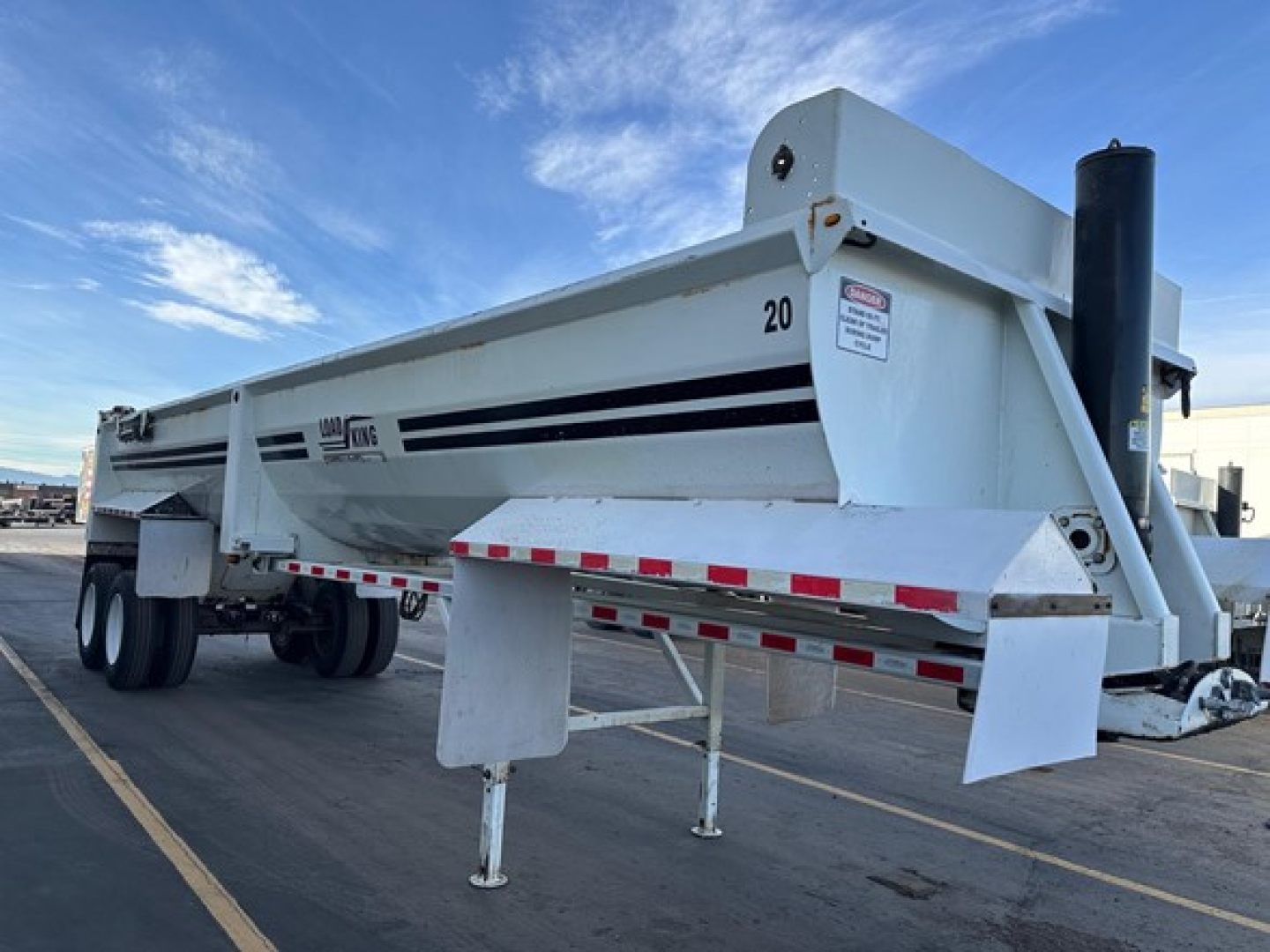 Load King RH32-29 dump trailer in profile view showing side panels, landing legs down, and hitch area with safety decals visible.