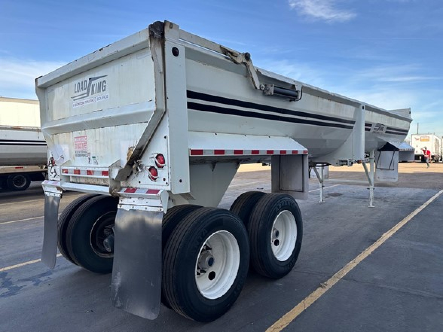 Load King RH32-29 dump trailer showing dual rear axles and white with black stripe branding, side markers, and rear taillights.