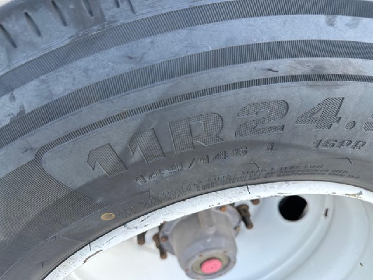 Truck trailer tire close-up showing tire brand/model markings: M^R24? and numbers 12.5/80R, plus a wheel hub with a pink center.