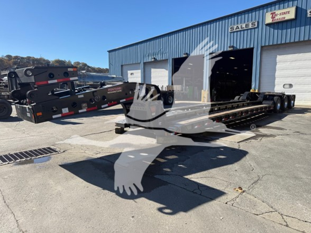 Lowboy trailer showing Fontaine Magnitude 60Hd Mdsr branding and equipment, with a second trailer and a warehouse in the background.