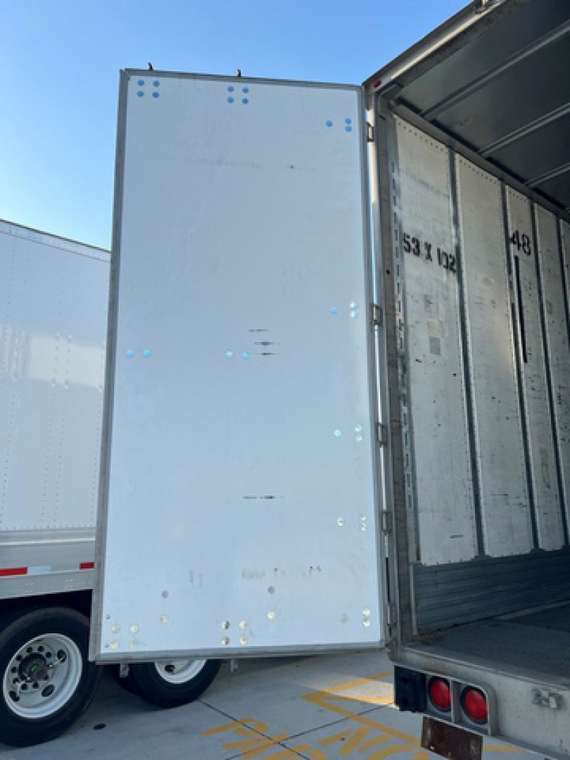 Trailer side door of a 2014 utility van in-view showing blank white panel and rear of an open trailer.