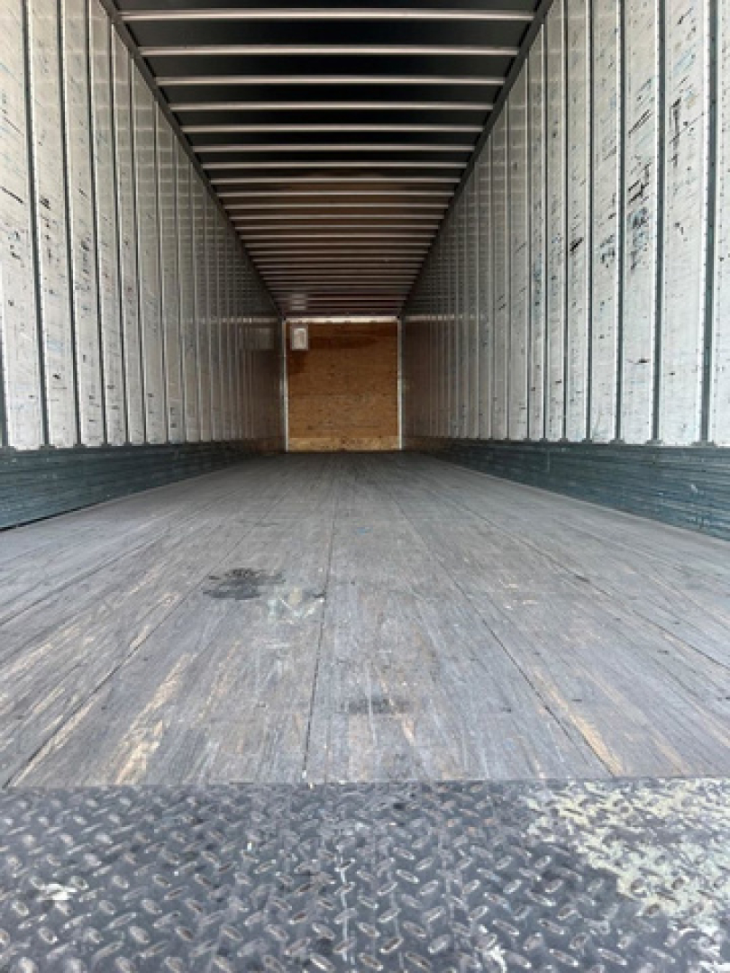 Trailer interior showing long empty cargo area with metal sidewalls and wooden floor planks, diamond plate at the threshold.