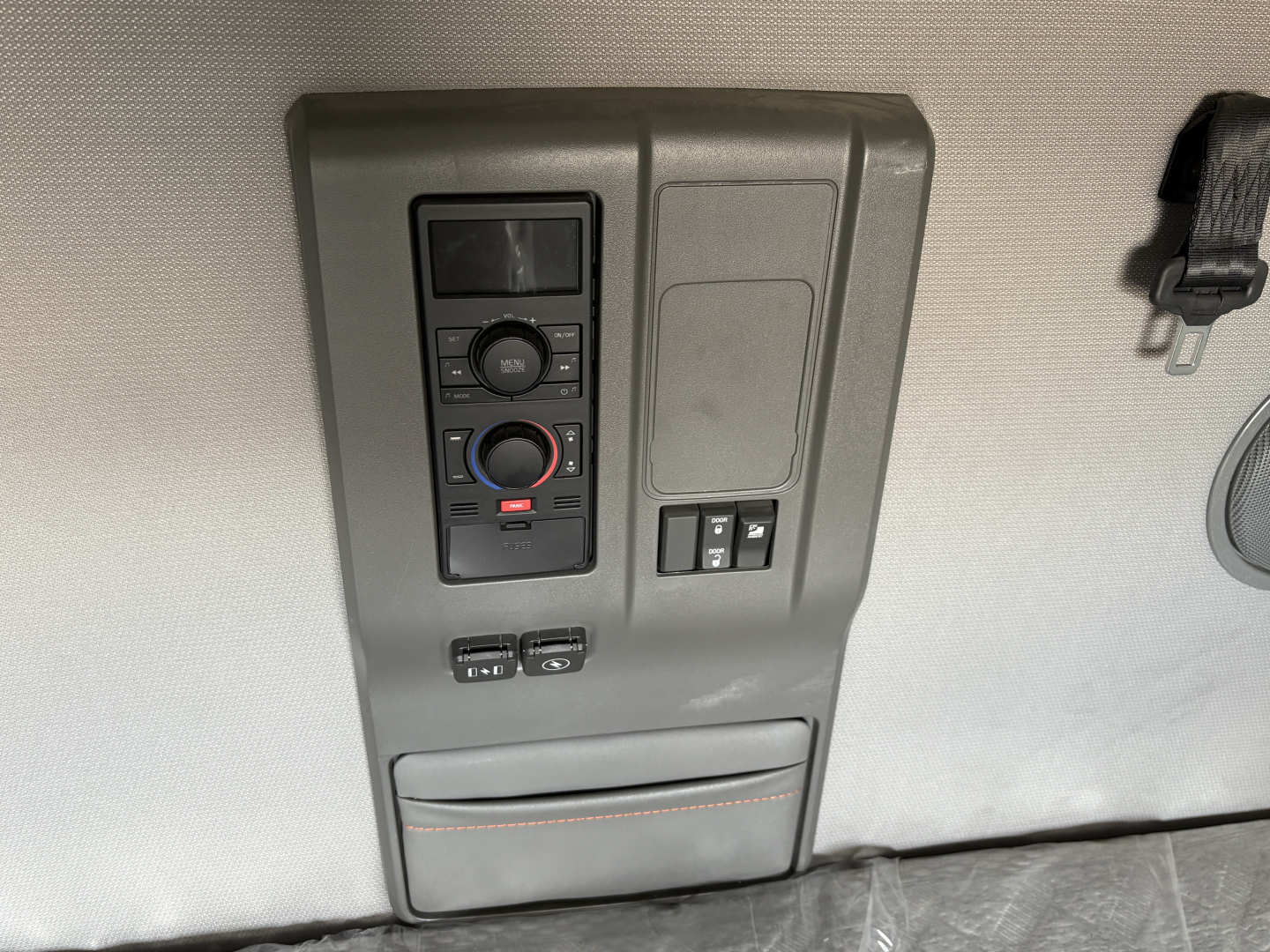 Control panel with digital display and circular knob, climate controls, and two small switches, mounted on light gray interior panel.