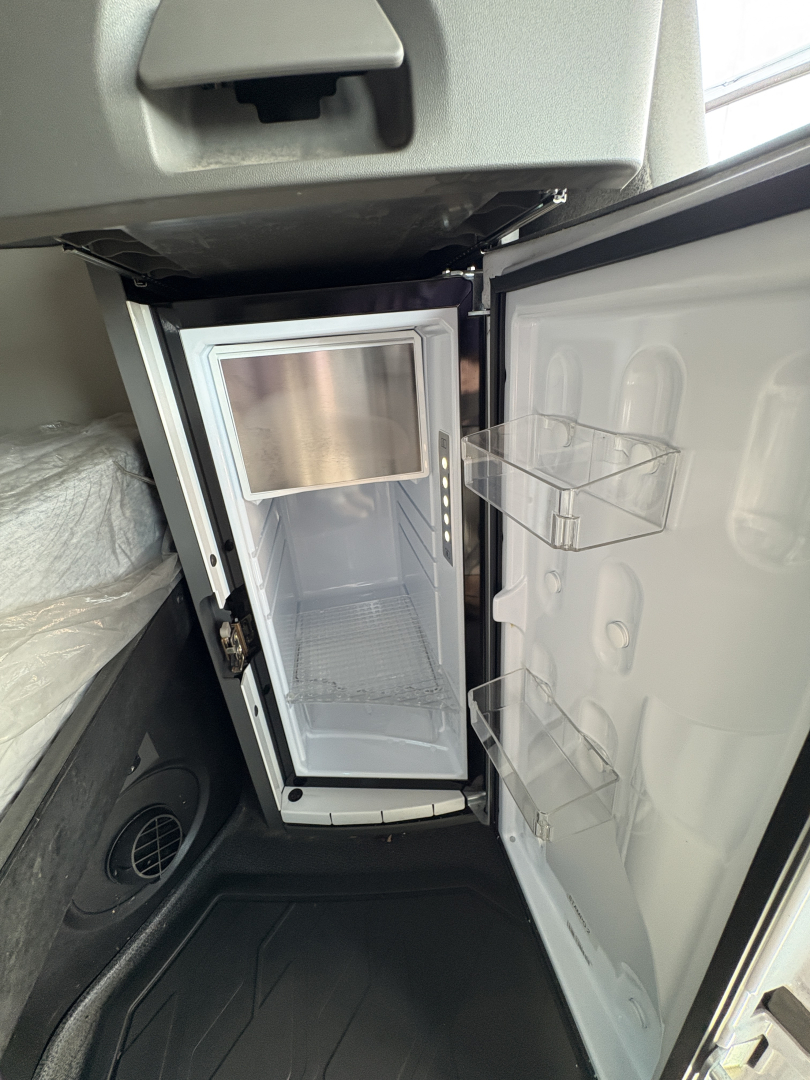 Mini fridge unit inside a Volvo VNL64T760 sleeper cab with an open door, showing shelves and interior.