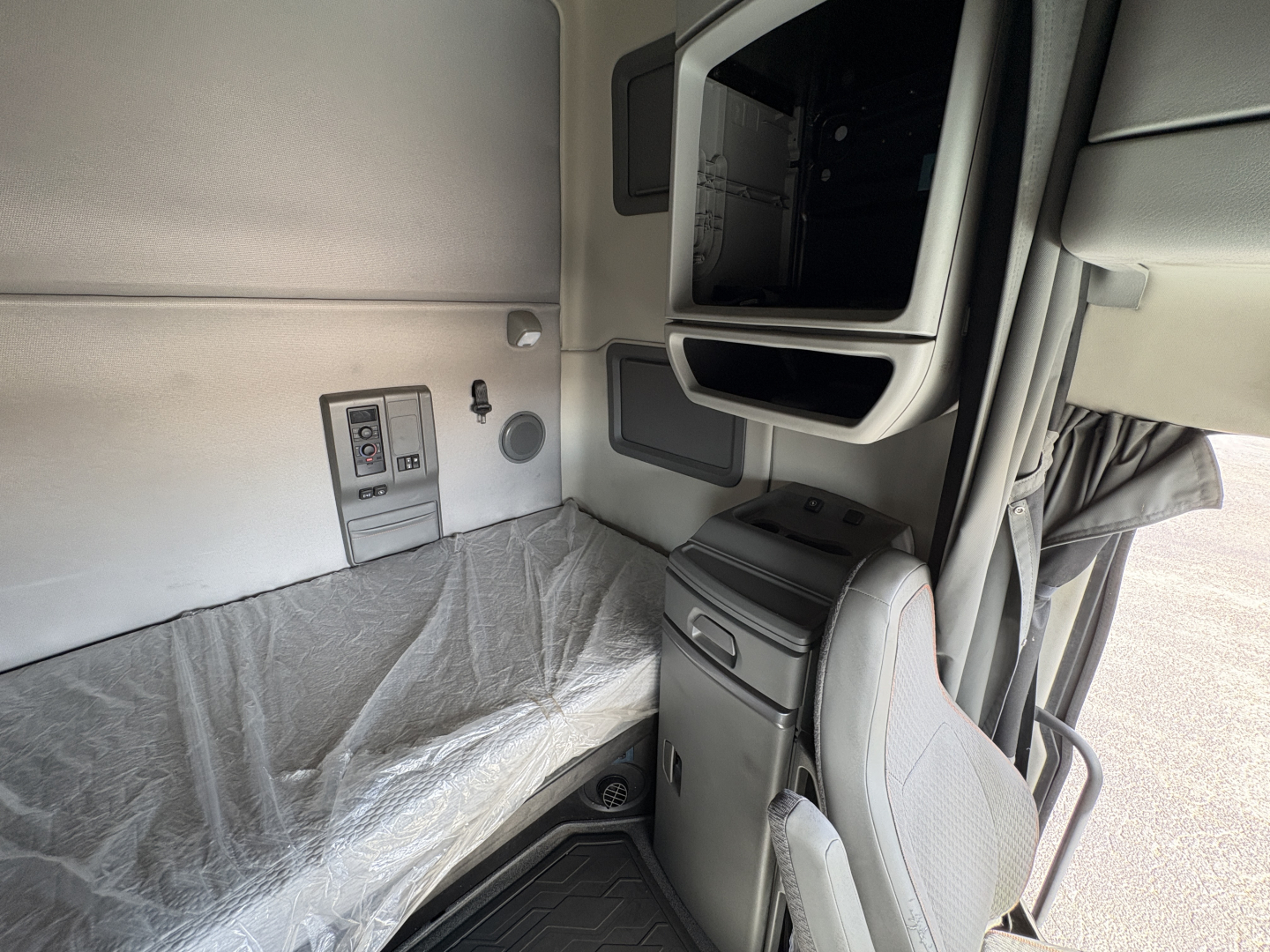Volvo VNL64T760 sleeper cab interior view showing side panel, storage compartment, and seat with plastic-covered berth area.