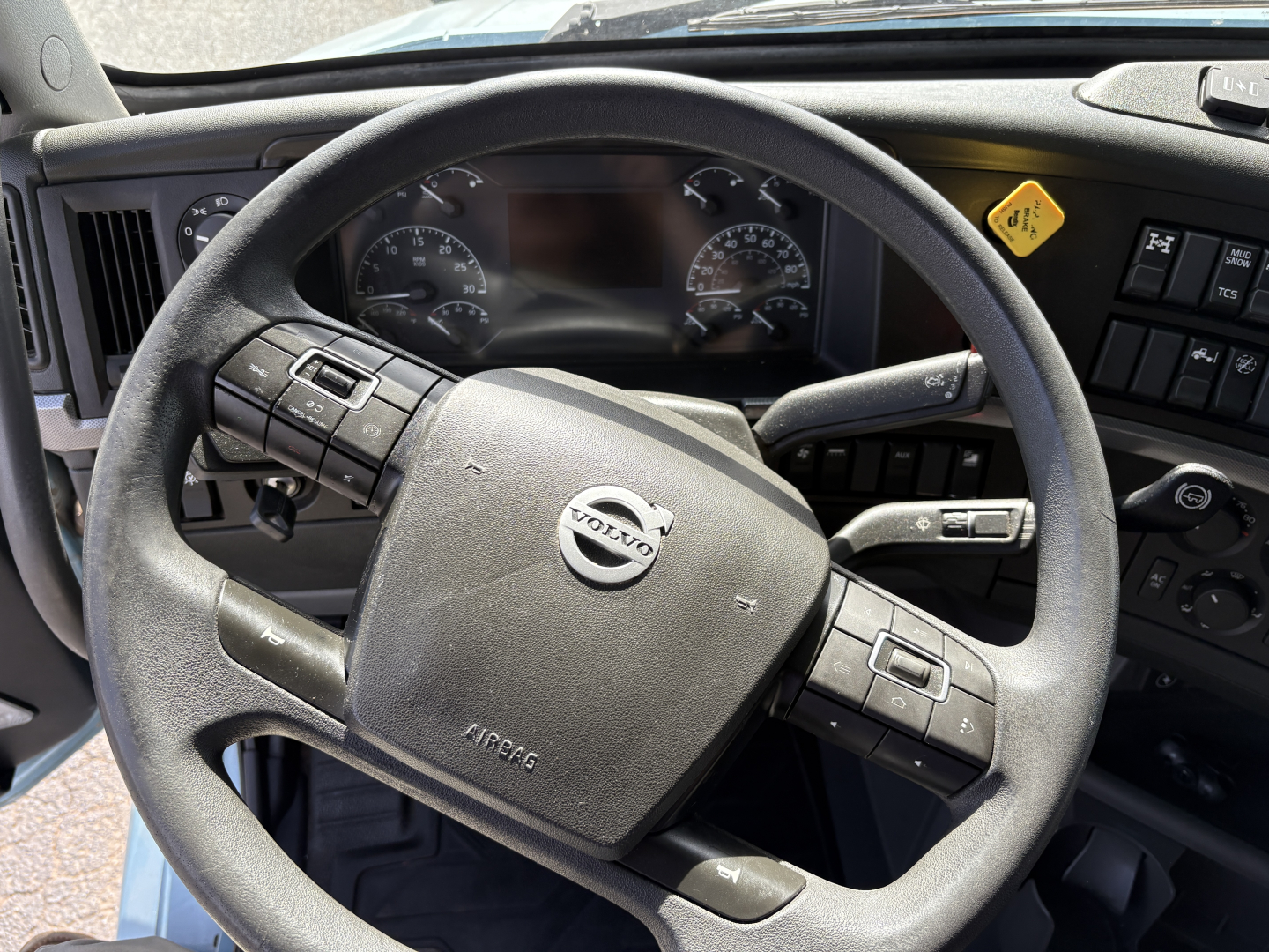 Volvo steering wheel and dashboard in truck cab showing Volvo logo on airbag module and steering controls.