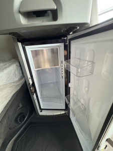Mini fridge unit inside a Volvo VNL64T760 sleeper cab with an open door, showing shelves and interior.