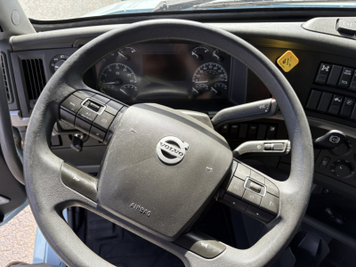 Volvo steering wheel and dashboard in truck cab showing Volvo logo on airbag module and steering controls.
