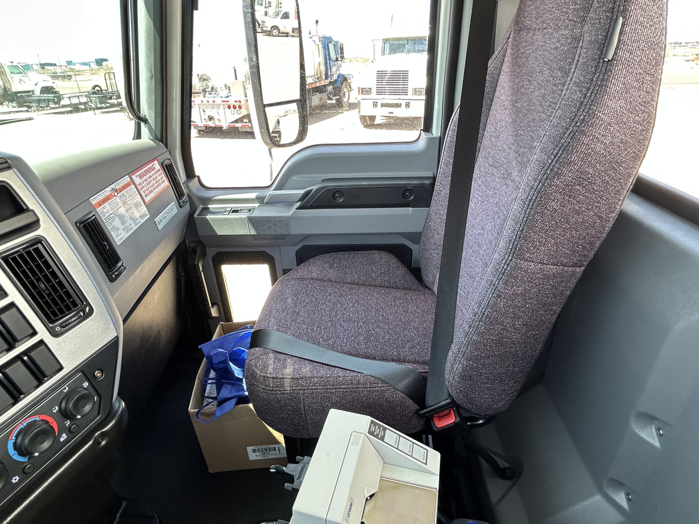 Seat and dashboard view inside a 2026 Mack MD7 truck cab showing fabric seat, steering area, and door panel.