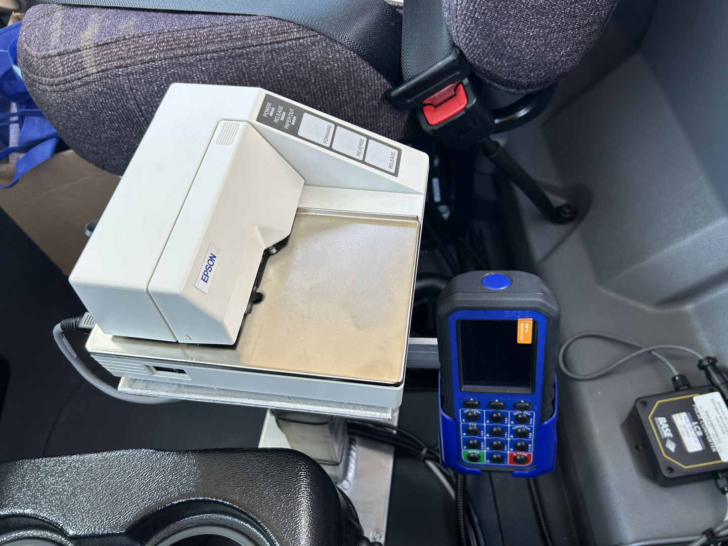 Cab interior of a 2026 Mack MD7 showing a payment terminal and a card reader mounted near the seat, with a small printer device and cables visible.