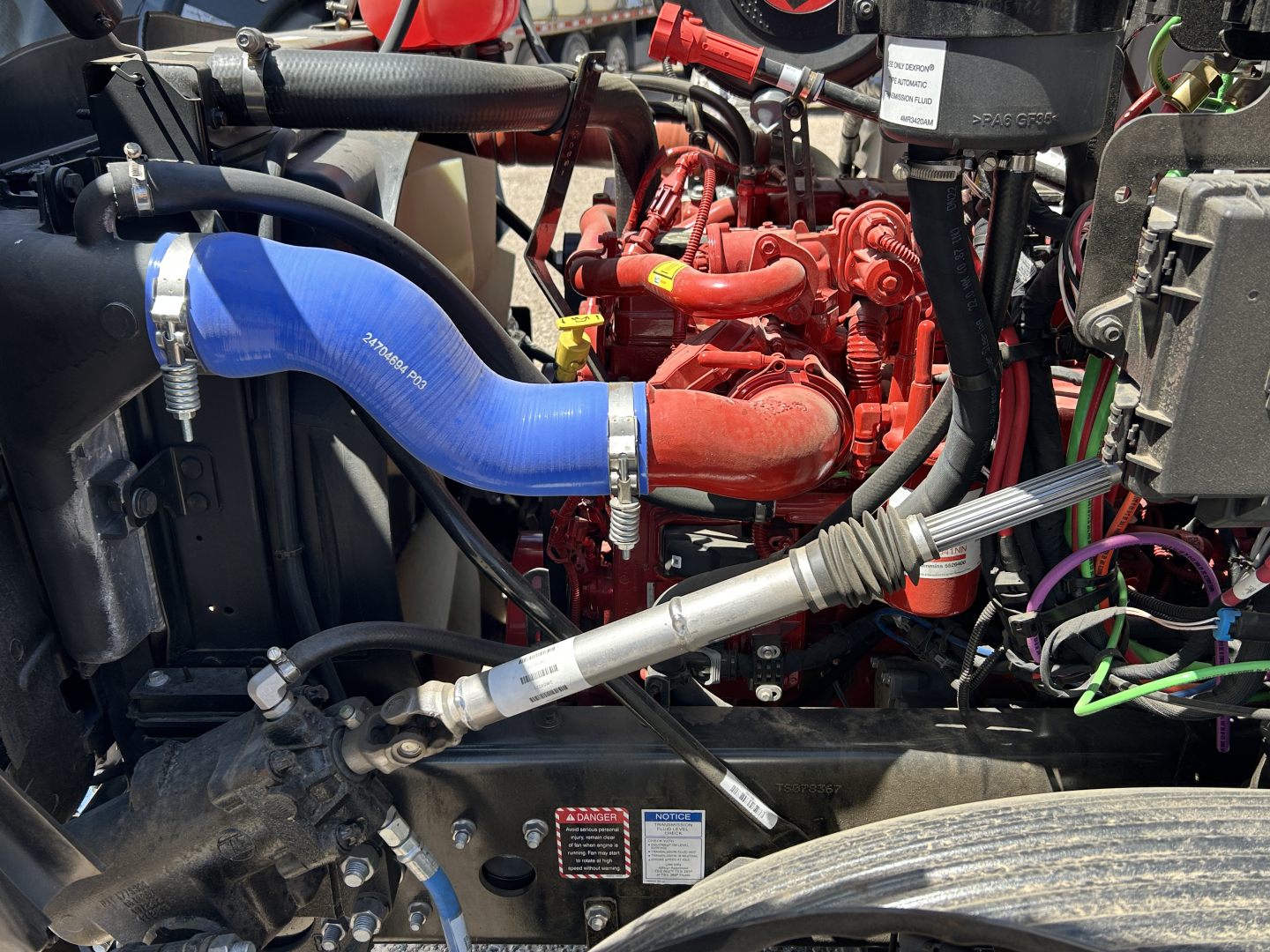 Mack MD7 engine bay showing blue silicone intercooler hose, red engine block, black radiator and various hoses and wiring harnesses.