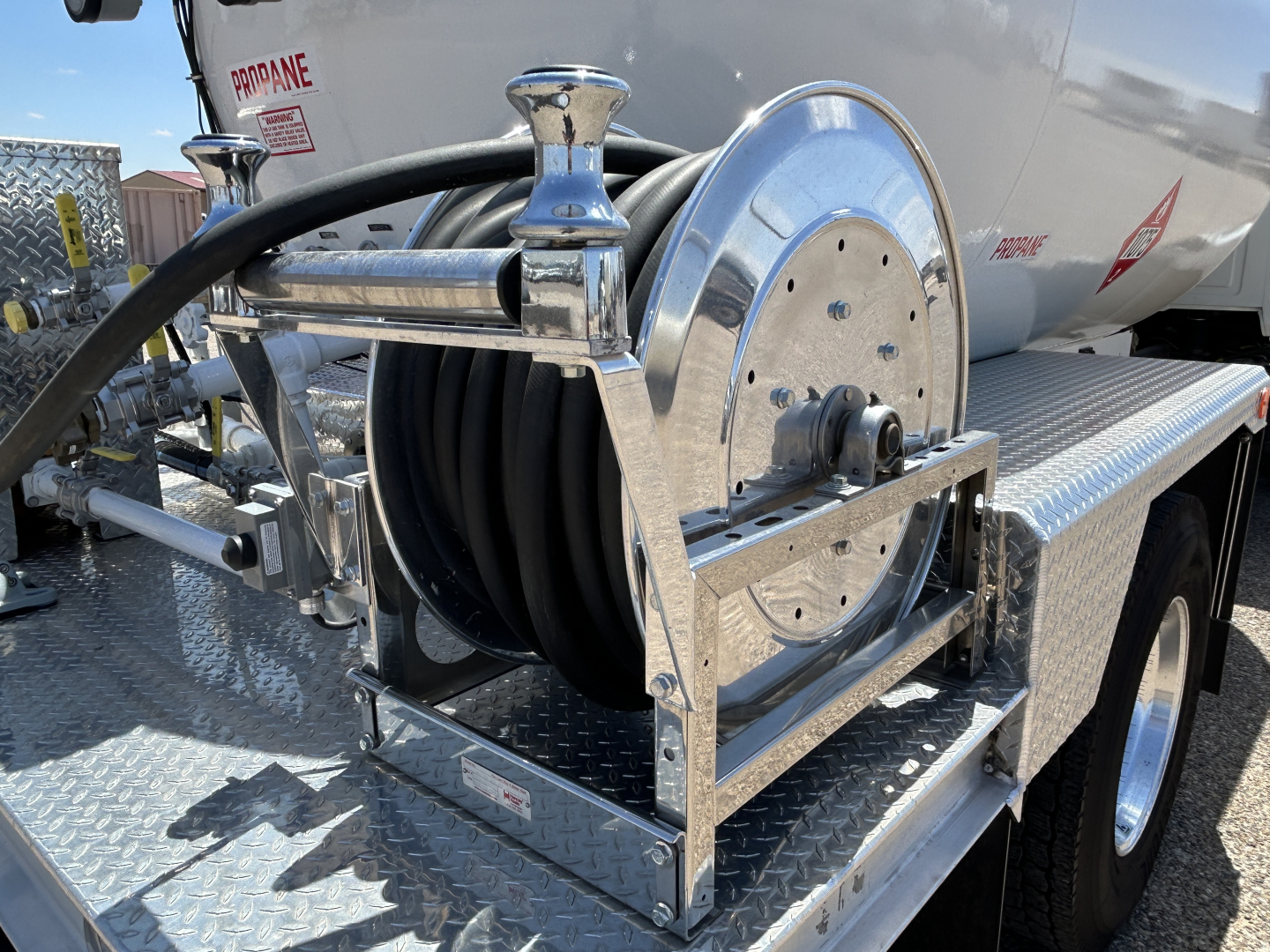 Aluminum hose reel mounted on side of tanker truck showing coiled hose and metal frame with diamond plate steps.