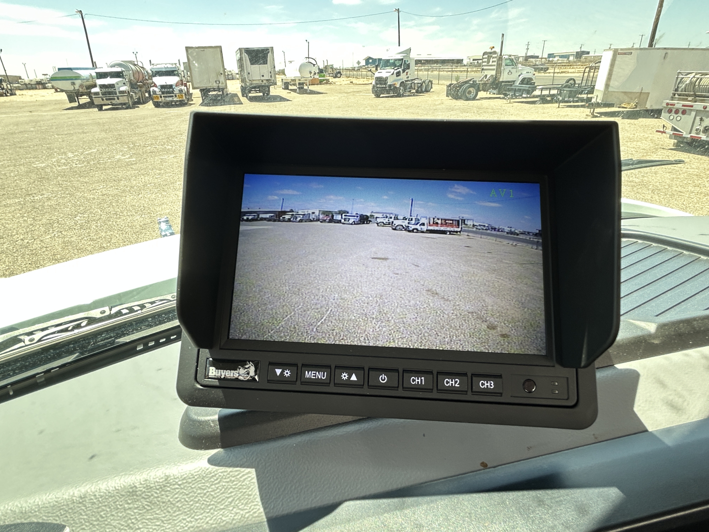 Monitor display in a Mack MD7 cab showing rear view camera image with control buttons below and dashboard surrounding.