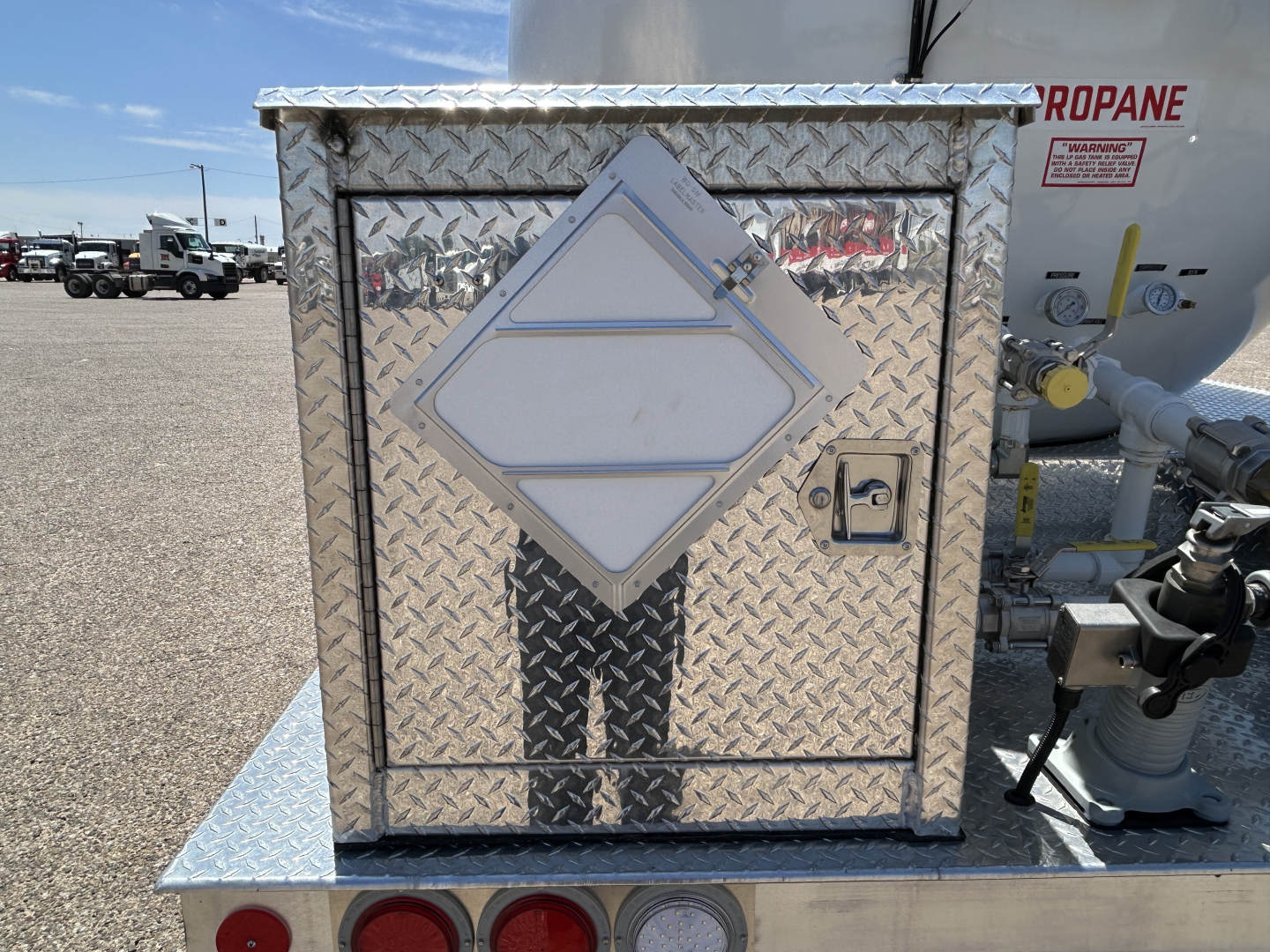 Diamond-plate storage box on Mack MD7 truck component with propane tank and valves in background.