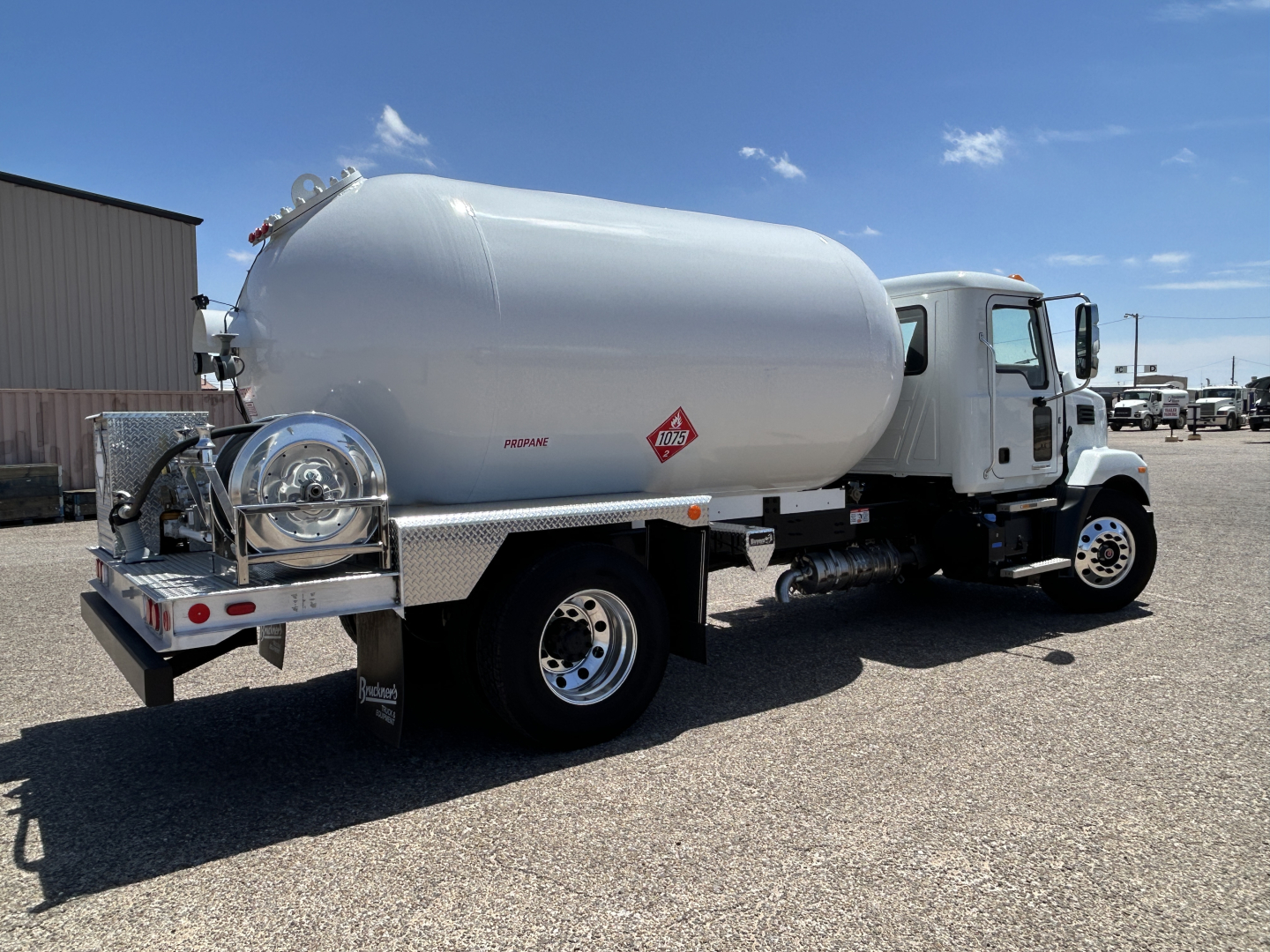 Tank truck with cylindrical white cargo tank mounted on a white Mack MD7 chassis, side view showing safe lines and fuel tank, clear blue sky.