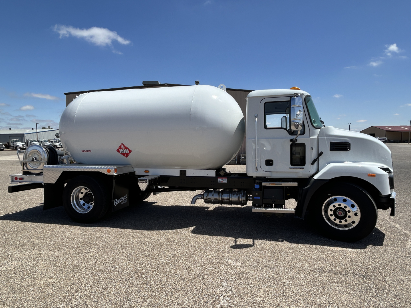 Tank truck side view showing cylindrical white fuel/propane tank mounted on a Mack MD7 chassis with cab, wheel rims, and tanker equipment.