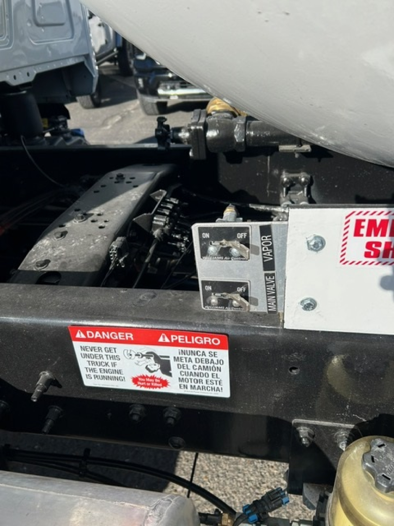 Truck chassis area with warning label and control switches visible under a tank, showing danger sticker and a dual switch panel.
