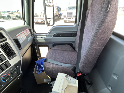 Seat and dashboard view inside a 2026 Mack MD7 truck cab showing fabric seat, steering area, and door panel.