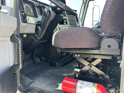 Truck interior showing driver's seat and dashboard of 2026 Mack MD7 with a red fire extinguisher on the floor by the entry.