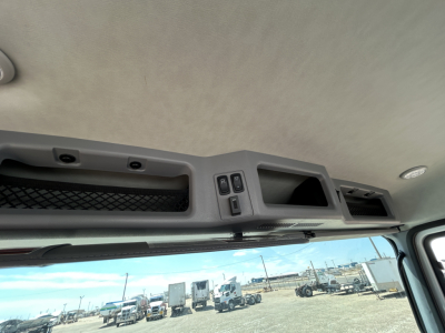Cab interior overhead console with storage compartments and switches, view through windshield to trucks and trailers in lot.