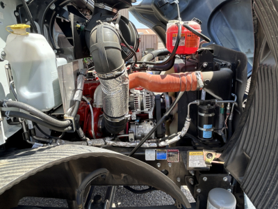 Engine bay of a 2026 Mack MD7 truck showing radiator coolant reservoir, air intake, hoses, alternator, and various engine components.