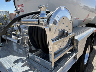 Aluminum hose reel mounted on side of tanker truck showing coiled hose and metal frame with diamond plate steps.