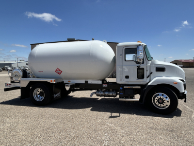Tank truck side view showing cylindrical white fuel/propane tank mounted on a Mack MD7 chassis with cab, wheel rims, and tanker equipment.