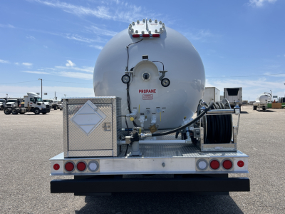 Propane tanker trailer rear view showing cylindrical tank with hoses, control gauges, and a diamond placard box on aluminum deck.