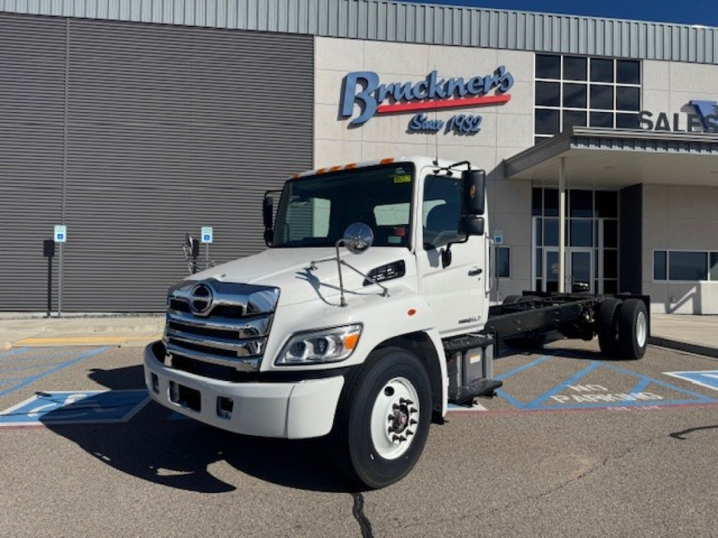 White 2025 Hino L7 cab chassis truck in showroom lot showing front and side view with Bruckner's sign in background.